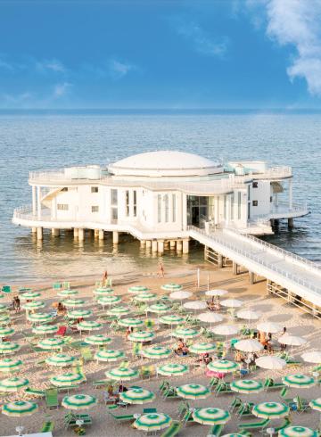 Spiaggia soleggiata con ombrelloni colorati e edificio sul mare.