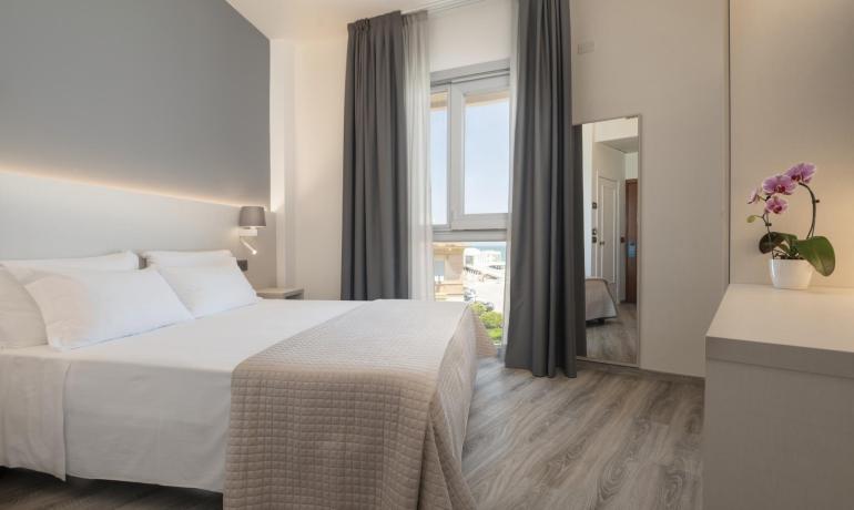 Camera moderna con letto matrimoniale e finestra luminosa.